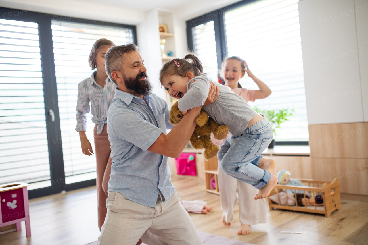 A father with three daughters indoors at home, playing on floor.