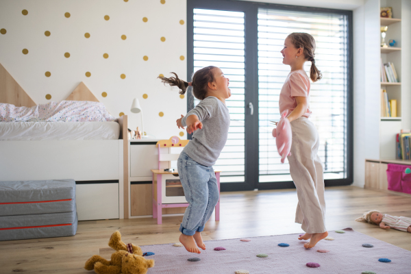 A portrait of girls sisters playing indoors at home, jumping.