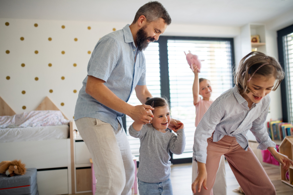 A father with three daughters indoors at home, playing and holding hands.