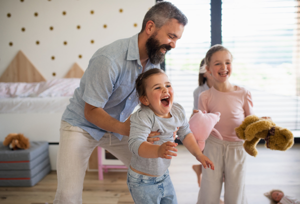 A father with three daughters indoors at home, having fun playing.