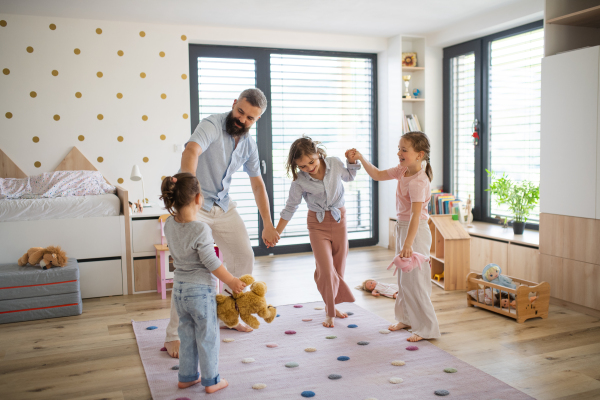 A father with three daughters indoors at home, playing and holding hands.