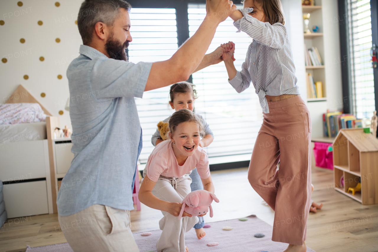 A father with three daughters indoors at home, playing on floor.