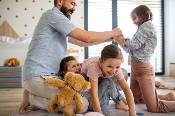 A father with three daughters indoors at home, playing on floor.