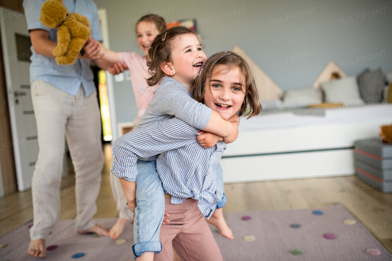 An unrecognizable father with three daughters indoors at home, playing and having fun.