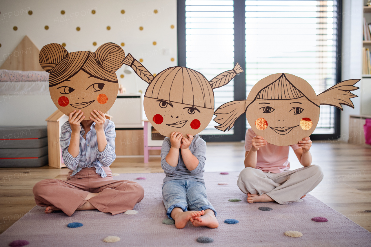 A portrait of three girls sisters indoors at home, playing.