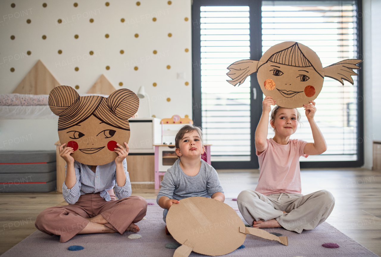 A portrait of three girls sisters indoors at home, playing.