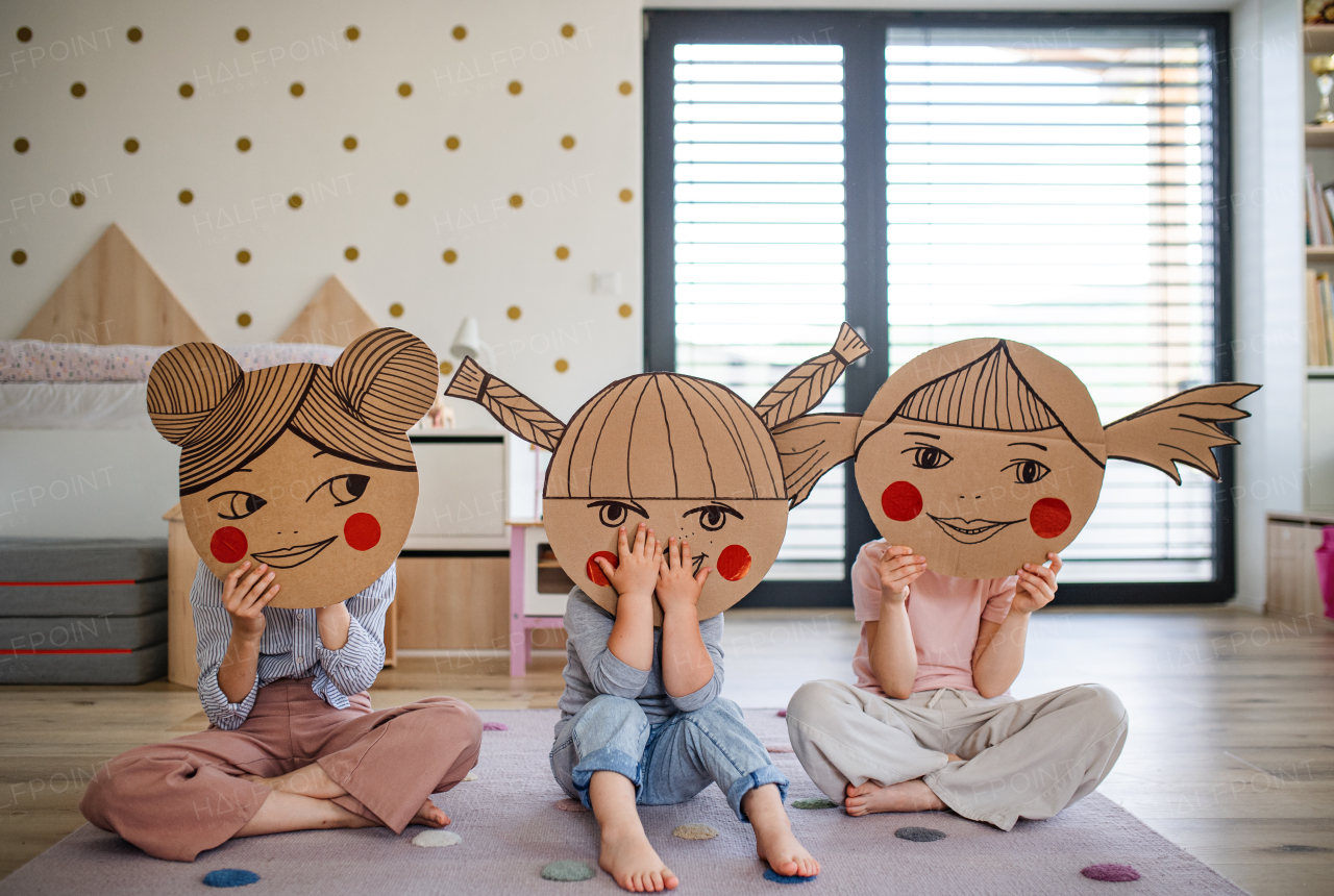 A portrait of three girls sisters indoors at home, playing.