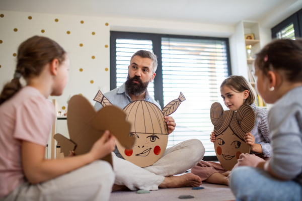 A father with three daughters indoors at home, playing on floor.