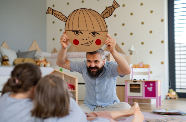 A father with three daughters indoors at home, playing on floor.