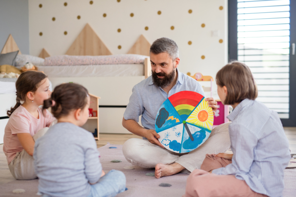 A father with three daughters indoors at home, playing on floor.