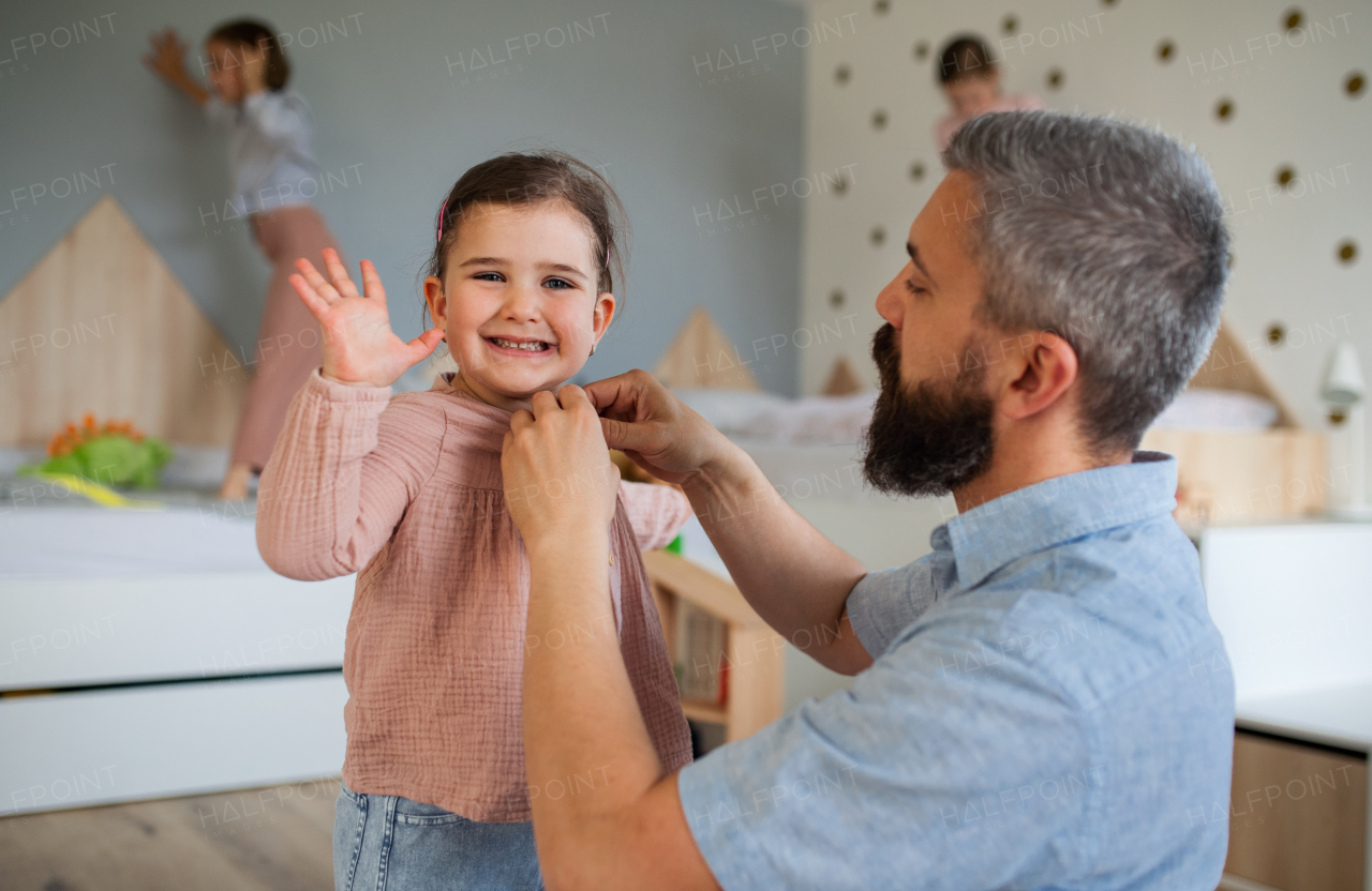 A father with three daughters indoors at home, helping to get dressed.