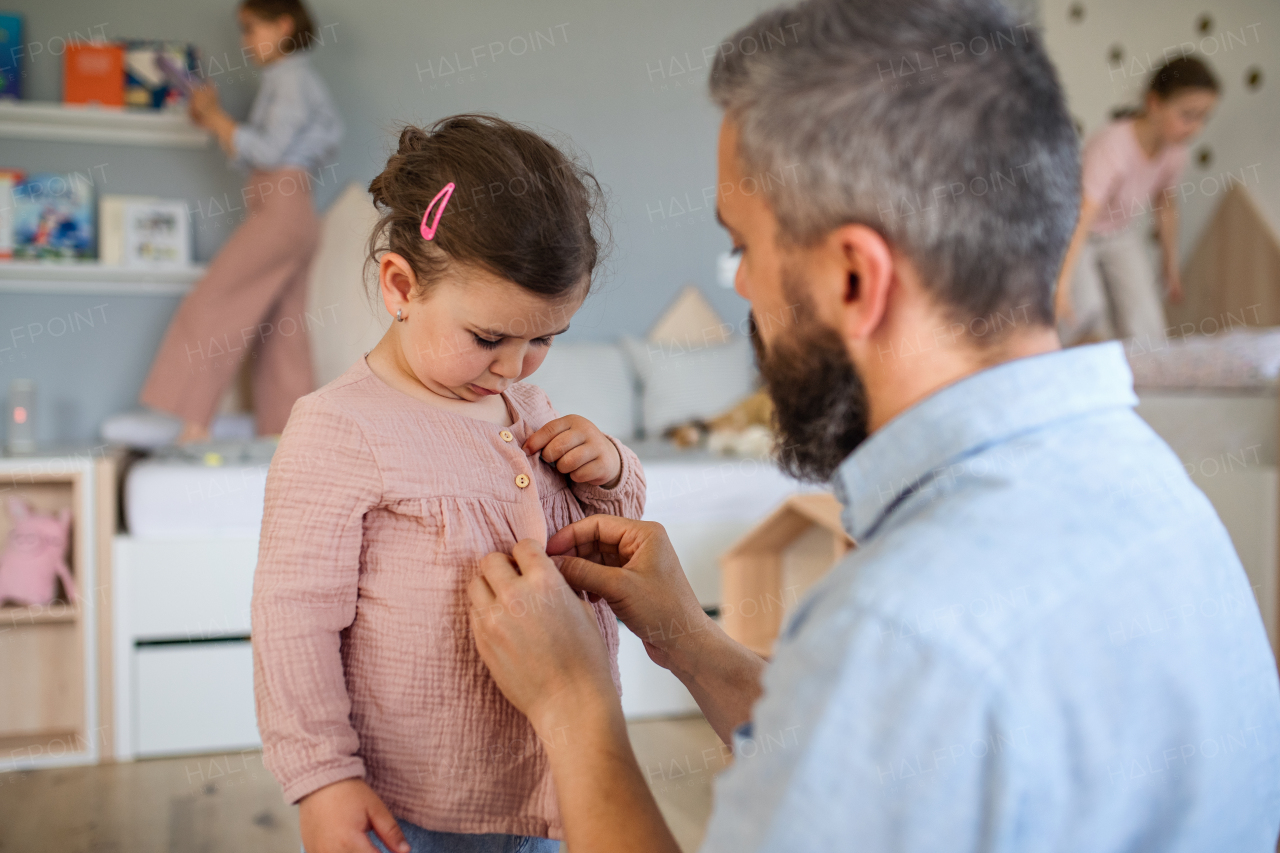 A father with three daughters indoors at home, helping to get dressed.