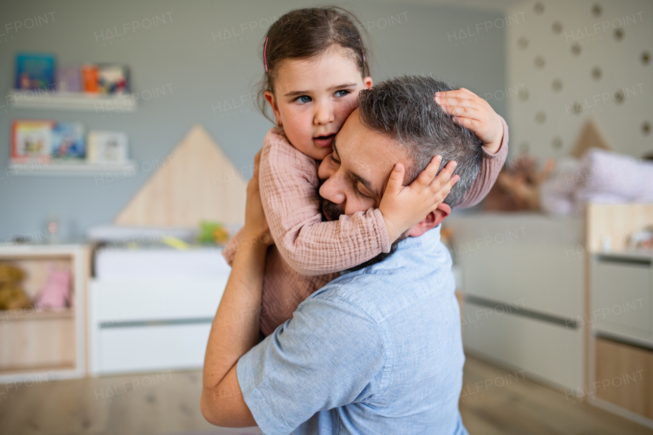 A happy father with daughter indoors at home, hugging.