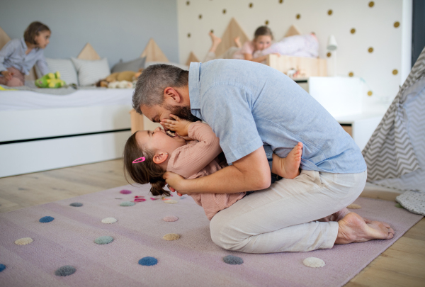 A father with daughters indoors at home, playing, laughing and having fun.