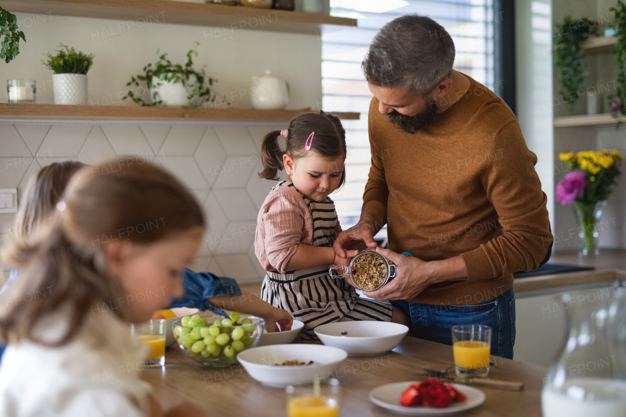 A father with three daughters indoors at home, eating breakfast in kitchen.