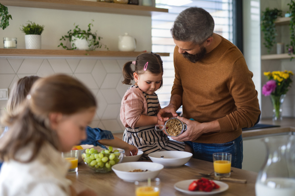 A father with three daughters indoors at home, eating breakfast in kitchen.