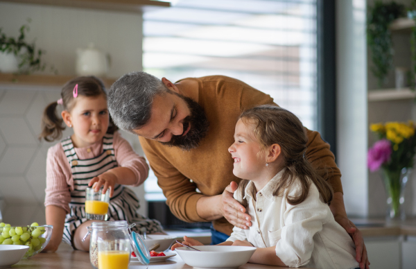 A father with three daughters indoors at home, eating breakfast in kitchen.