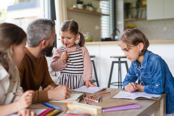 A father with three daughters indoors at home, drawing pictures.