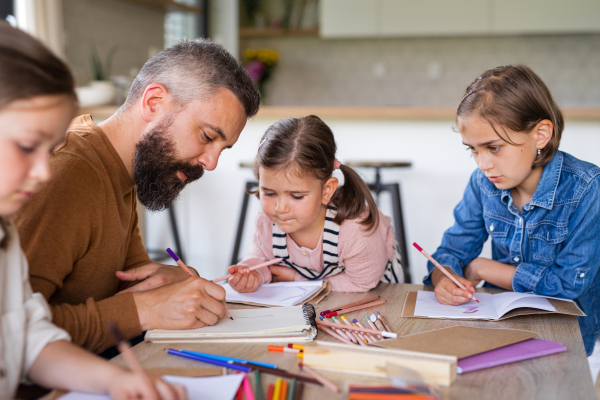 A father with three daughters indoors at home, drawing pictures.