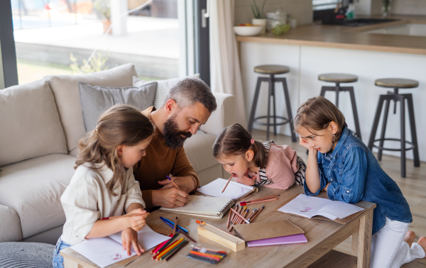 A father with three daughters indoors at home, drawing pictures.