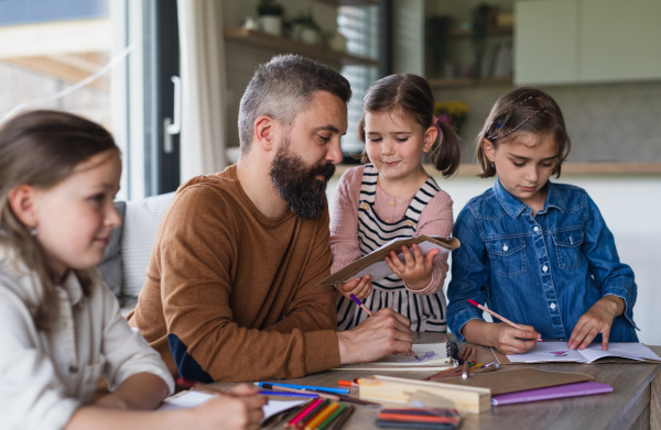 A father with three daughters indoors at home, drawing pictures.