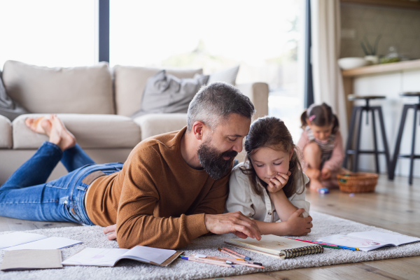 Mature father with daughters indoors at home, drawing pictures on floor.