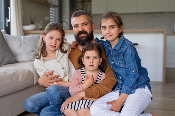 A father with three daughters indoors at home, looking at camera.