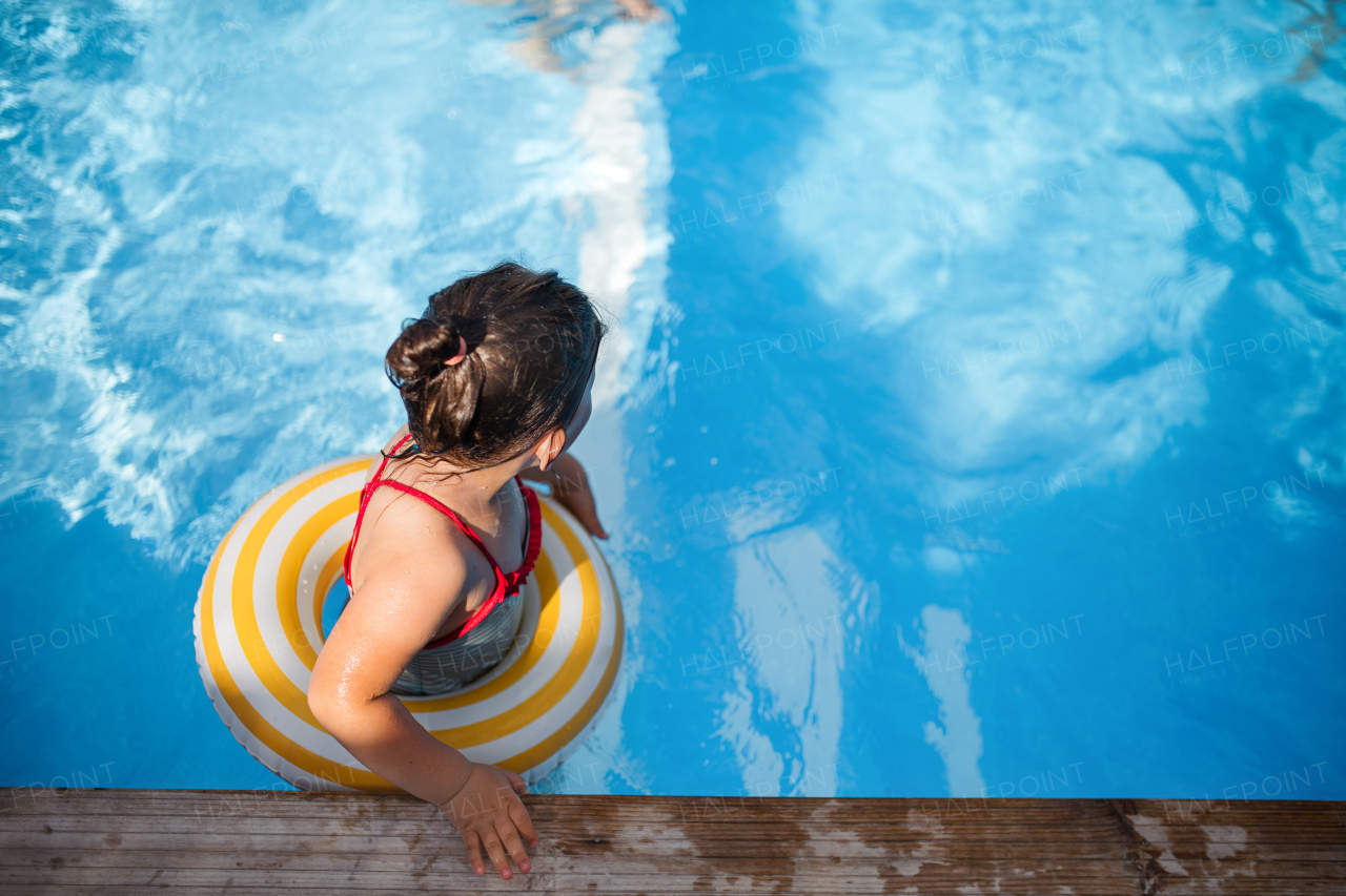 A top view of small girl outdoors in the backyard, with rubber ring in swimming pool.