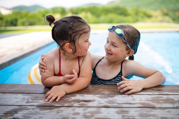 Portrait of two small girls sisters outdoors in the backyard, talking in swimming pool.