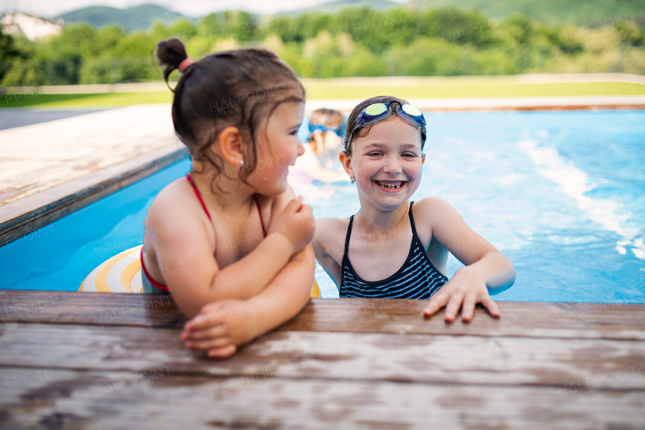 Portrait of two small girls sisters outdoors in the backyard, talking in swimming pool.