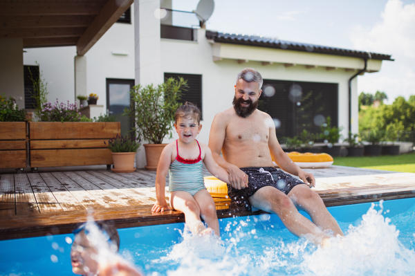 A father with three daughters outdoors in the backyard, sitting by swimming pool.