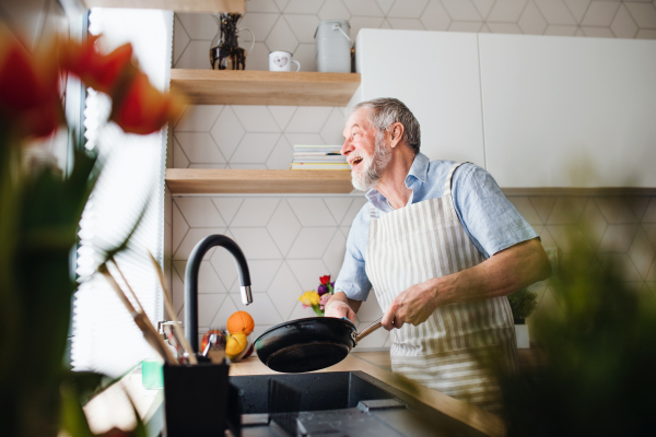 A senior man indoors in kitchen at home, washing up a pan after cooking.