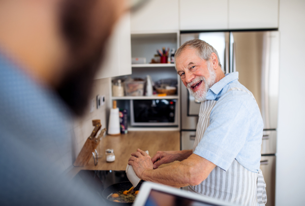 A happy senior man indoors in kitchen at home, cooking.