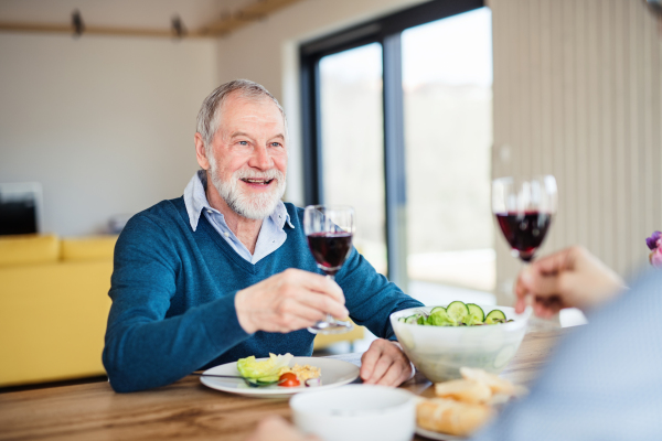 An adult hipster son and senior father sitting at the table indoors at home, eating light lunch.