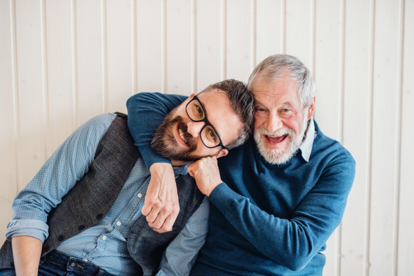 A portrait of adult hipster son and senior father sitting on floor indoors at home, having fun.