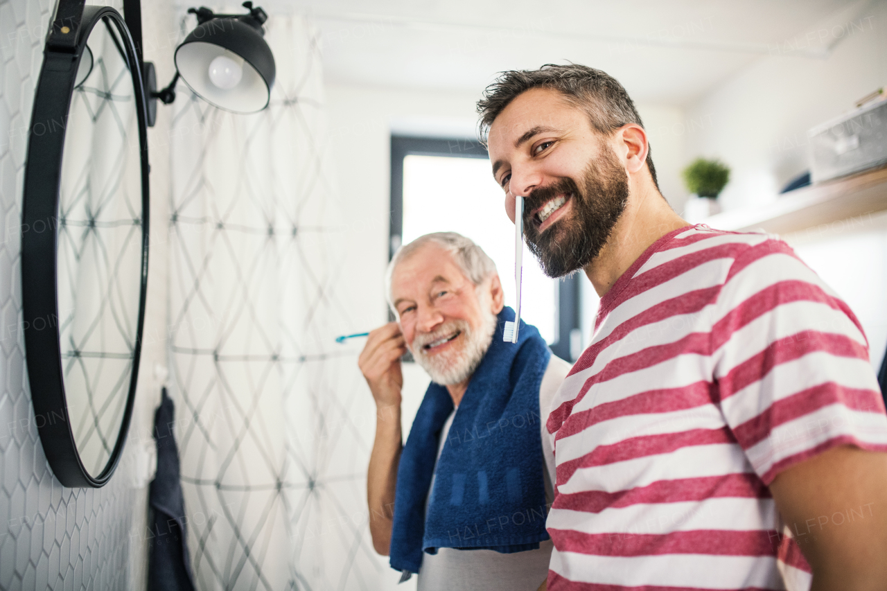 A cheerful adult hipster son and senior father in bathroom indoors at home, having fun.