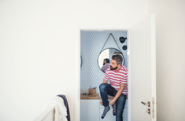 An adult hipster man getting dressed in brahroom indoors at home. Copy space.