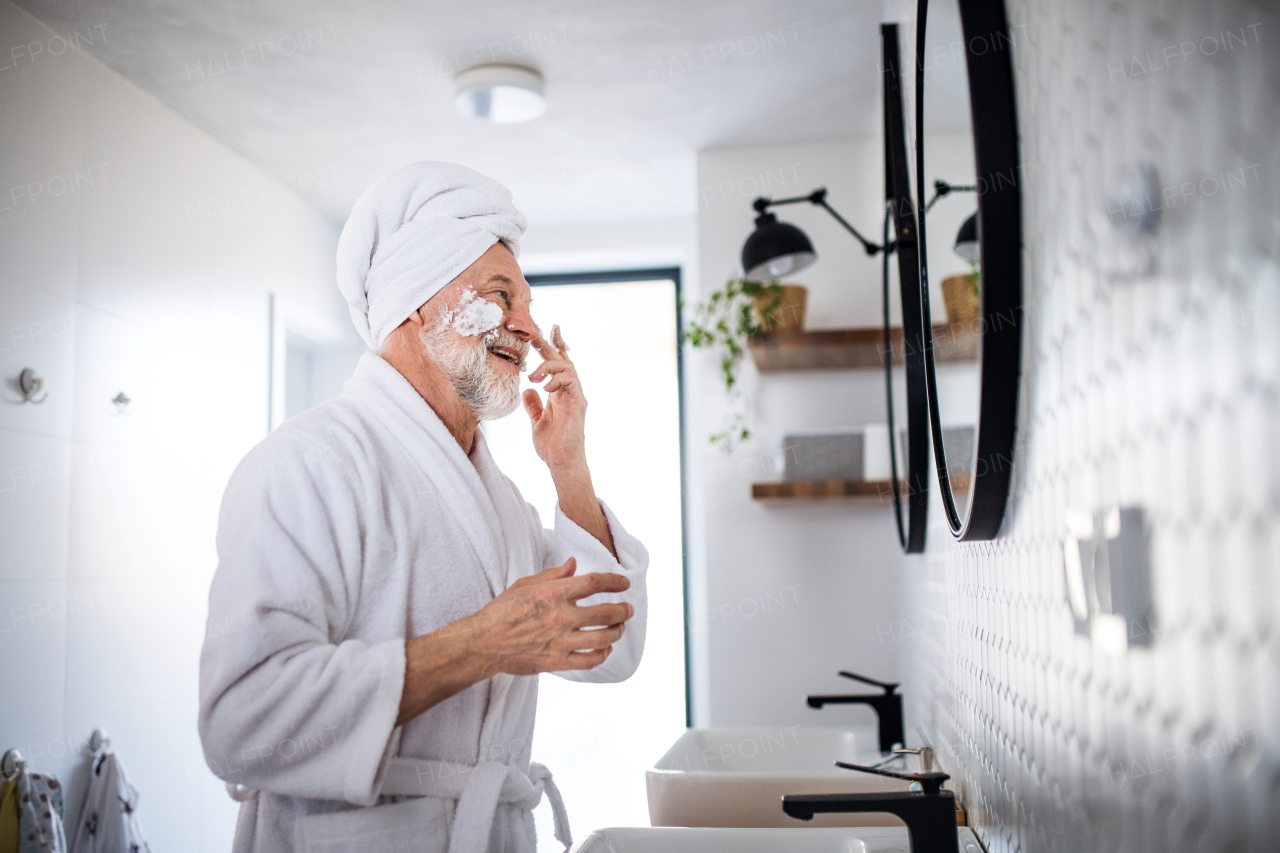 A senior man doing morning routine in bathroom indoors at home, looking in mirror. Copy space.