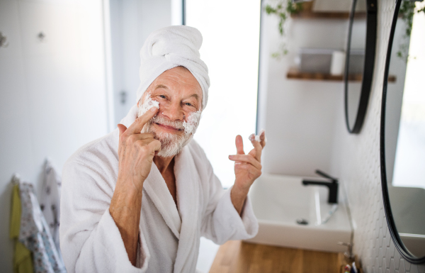 A senior man doing morning routine in bathroom indoors at home, looking at camera.