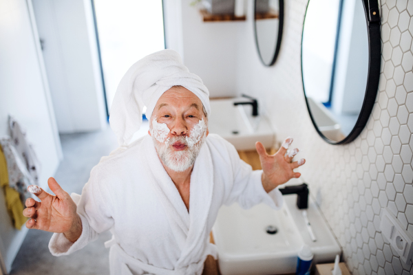 A senior man doing morning routine in bathroom indoors at home, looking at camera.