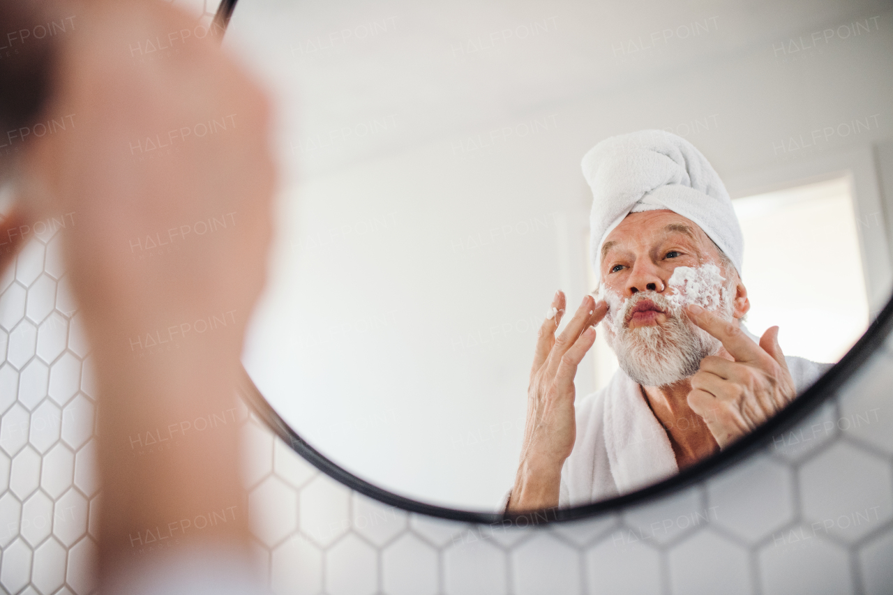 A senior man doing morning routine in bathroom indoors at home, looking in mirror. Copy space.