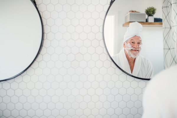 A senior man doing morning routine in bathroom indoors at home, looking in mirror. Copy space.