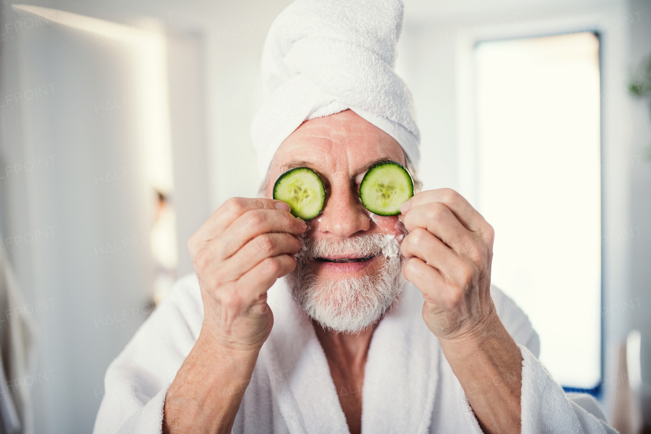 A senior man with cucumber on front of his eyes in bathroom indoors at home.