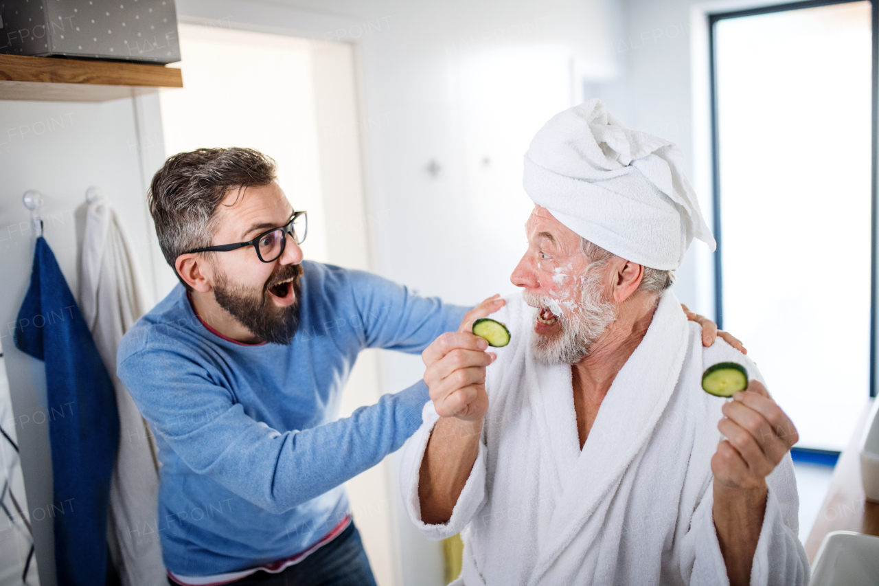 A cheerful adult hipster son and senior father in bathroom indoors at home, having fun.