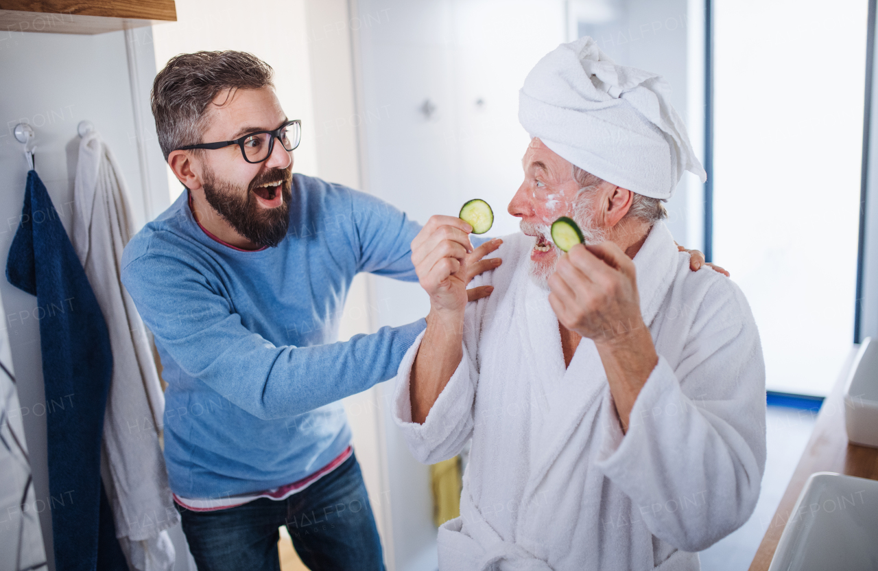 A cheerful adult hipster son and senior father in bathroom indoors at home, having fun.