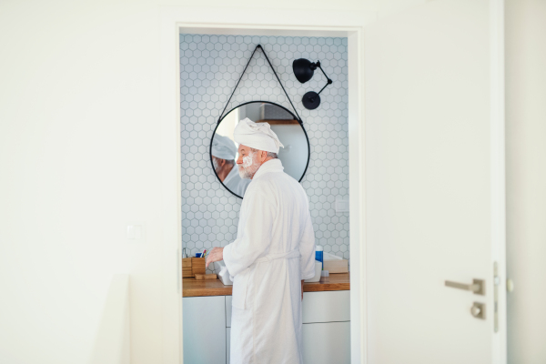 A senior man doing morning routine in bathroom indoors at home, looking in mirror. Copy space.