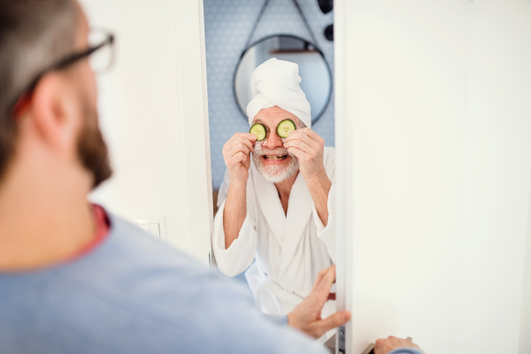 A cheerful adult hipster son and senior father in bathroom indoors at home, having fun.