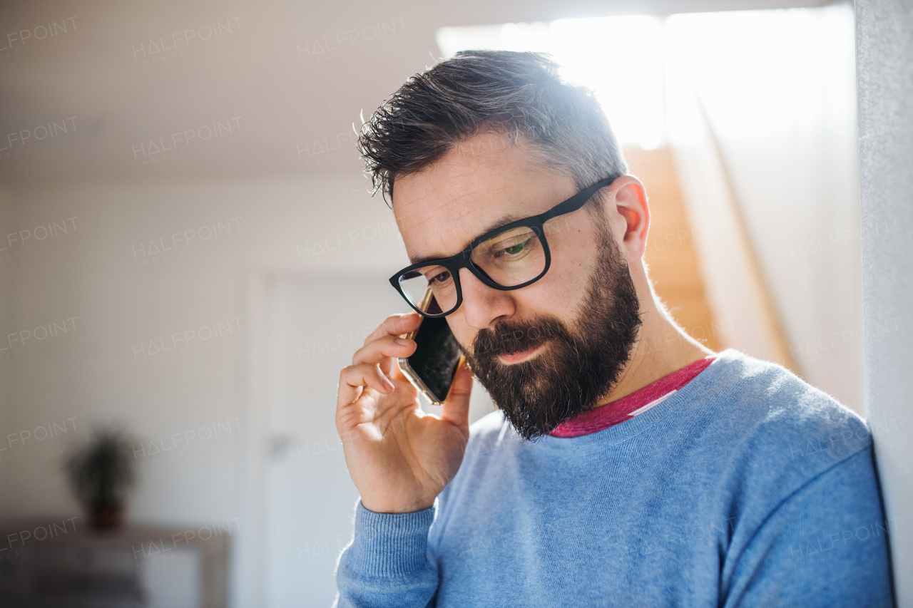 A hipster man with smartphone standing indoors at home, making a phone call.