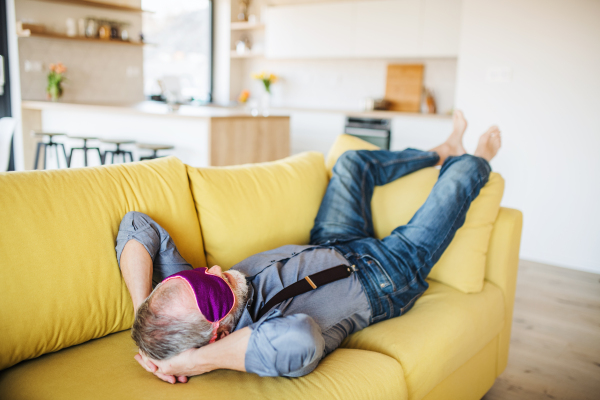 A senior man with eye mask lying on sofa indoors at home, relaxing.