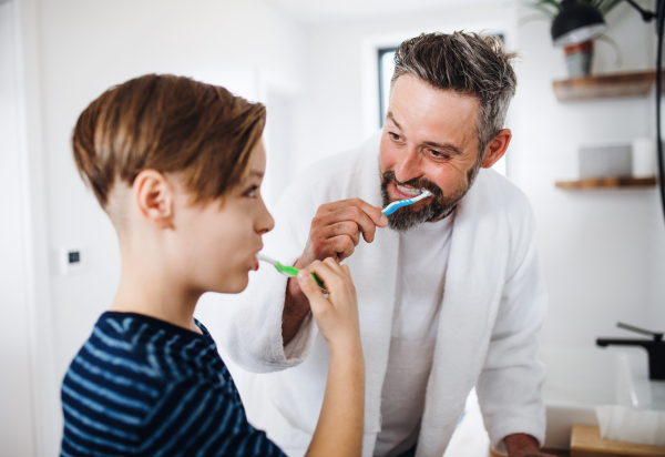 A mature father with small son in the bathroom in the morning, brushing teeth.